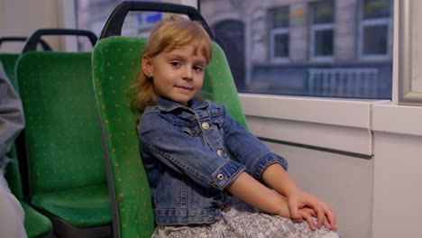 attractive child girl passenger riding at public modern bus or tram transport, looking out window