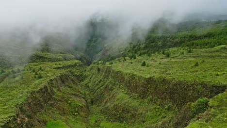 Foggy-aerial-view-of-Lagoa-do-Fogo's-lush-green-valley-surrounded-by-mountains-and-mist