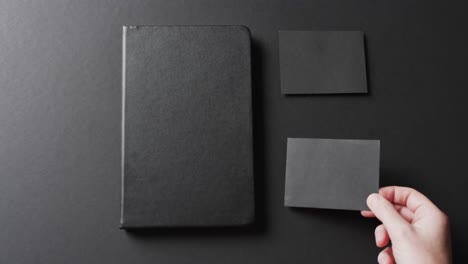 video of caucasian woman putting black paper cards with copy space and notebook on black background