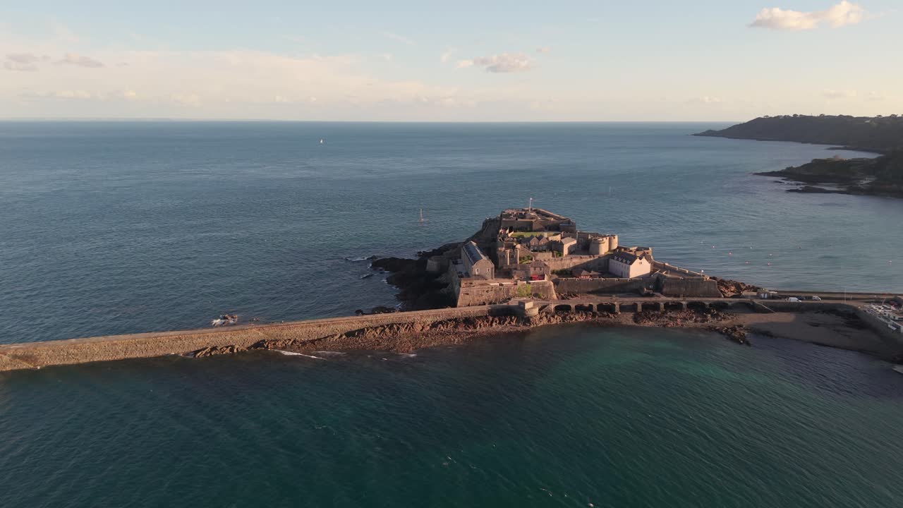 St Peter Port Harbour entrance Guernsey sweeping drone footage from lighthouse to Castle Cornet in golden hour with catamaran entering the harbour on calm clear sunny afternoon