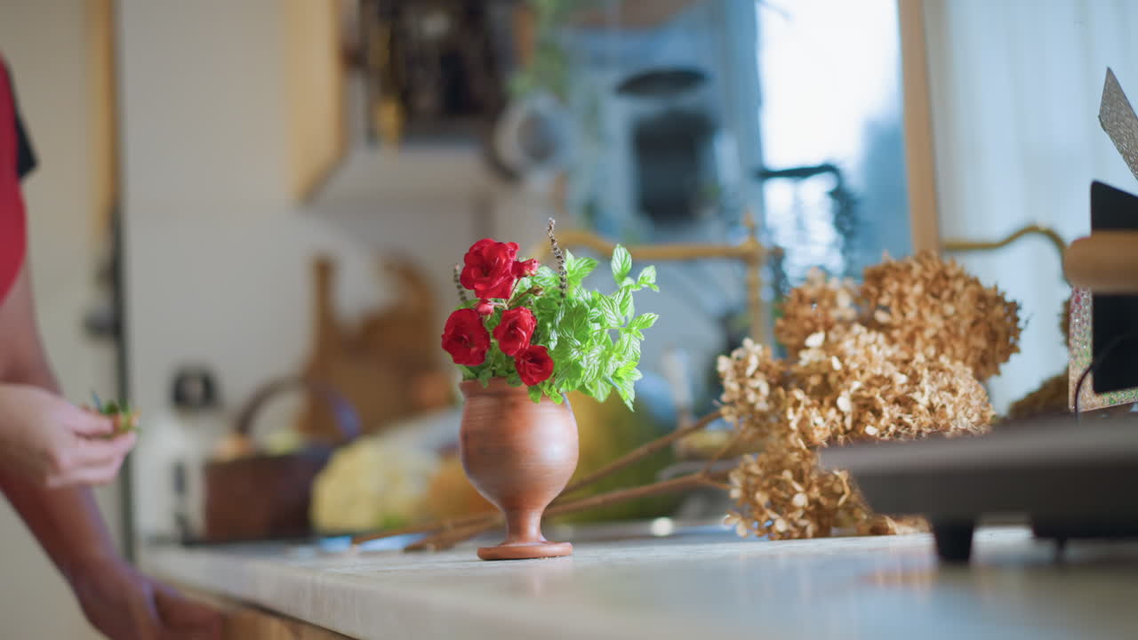 Ein Hauskoch arrangiert Blumen im Innenbereich. Hell beleuchtete Küche, in der eine Person Blumen an der Theke vorbereitet. Gemütliche häusliche Umgebung, die eine Person zeigt, die in einer sonnendurchfluteten Küche mit Blumen dekoriert.