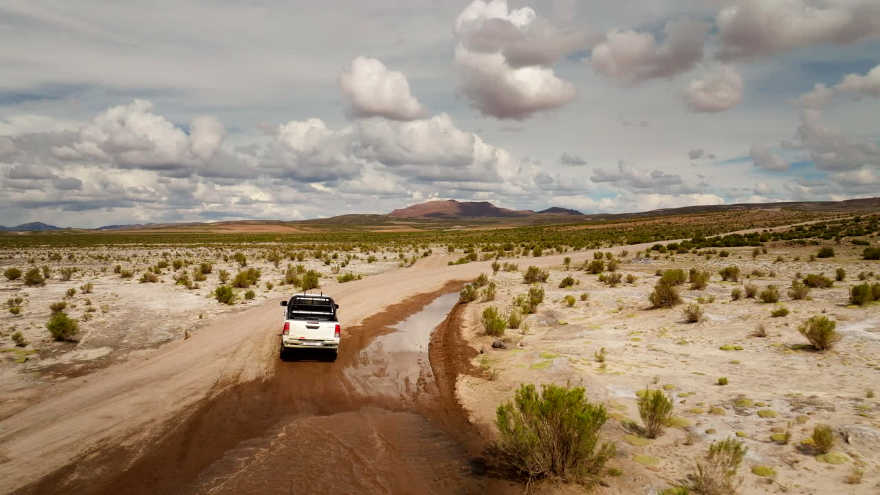 Pickup truck driving on remote dirt road through Siloli Desert, Bolivia. Aerial drone at low altitude