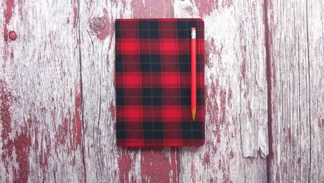 red plaid notebook with pencil on wooden table