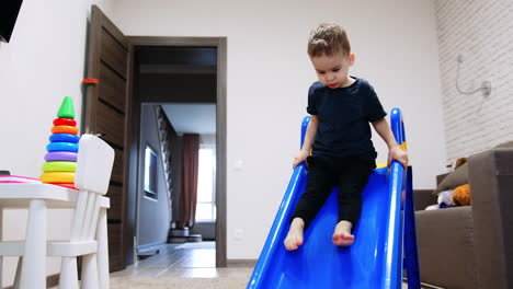 little toddler boy sitting on the slide. smiling baby boy goes down slowly. fun time at home.
