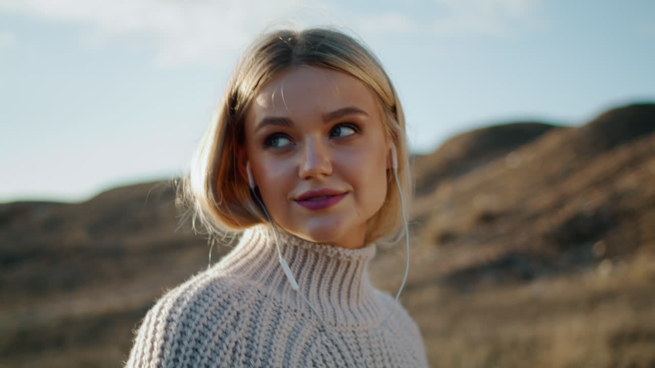 Blond model nyder musik i en efterårsdal, portræt. Studerende går på mark.