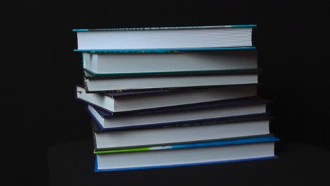 gorgeous spinning footage of colorful hardcover books in a pile on top of each other while camera spins around them. books with white pages are on a dark black studio background on display under light