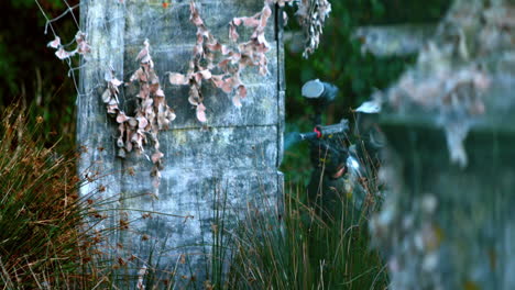 man shooting his paintball gun crouching in the grass