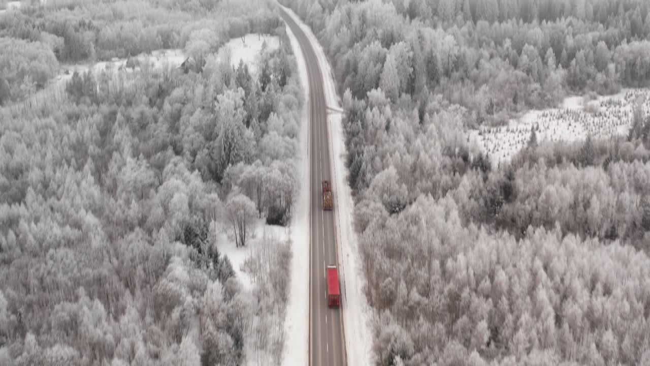 Fast pace reveal drone shot from asphalt highway with two trucks driving in countryside landscape on a winter day. Hoar frost on trees.