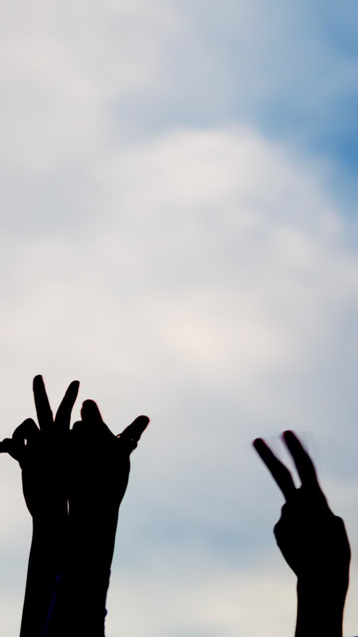 Silhouette on white of hands gesturing victory with sky background