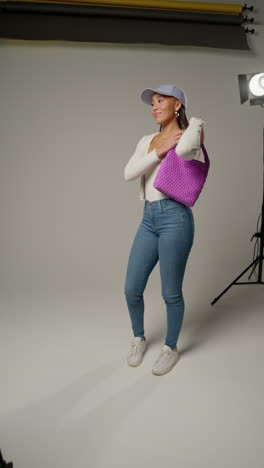 video vertical de una influyente femenina de las redes sociales produciendo contenido generado por el usuario en el estudio de modelado bolsa púrpura