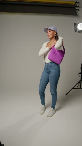 vertical video of female social media influencer producing user generated content in studio modelling purple bag