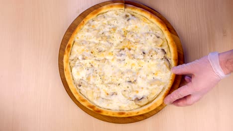 el cocinero corta la pizza con setas, setas y queso en una tabla de madera en la mesa.
