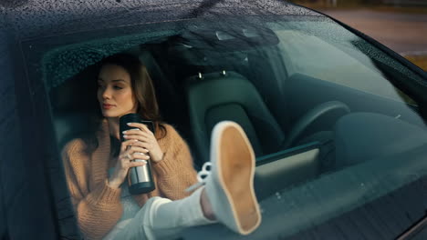 woman relaxing in car with mug and feet on dashboard