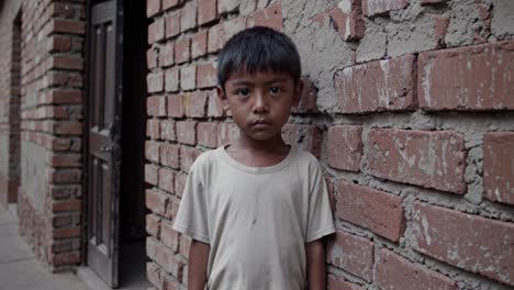 sad young boy standing near brick wall, wearing dirty t shirt, expressing loneliness and vulnerability through contemplative gaze and somber demeanor