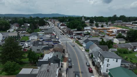 traffic on main street of american town with parking lot for yellow american school buses. cloudy day in middletown, pennsylvania. aerial landing shot. gas station and church in center