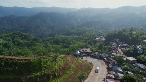 Idyllic-Aerial-View-of-a-Philippine-mountainside-village-town-with-winding-roads-and-facing-a-vast,-tropical-rainforest-during-summertime