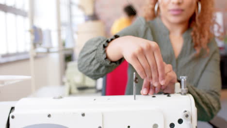 diseñadora de moda de dos razas enhebrando una máquina de coser en el estudio, en cámara lenta