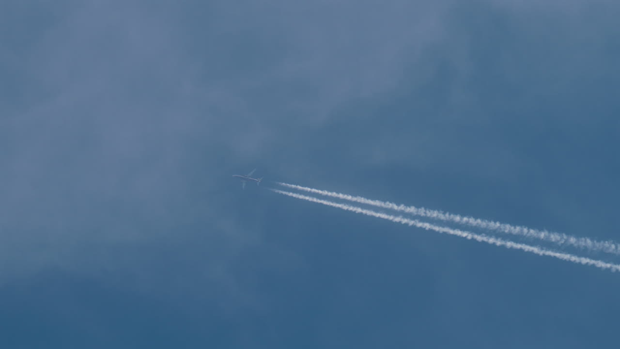 Airplane flying high above leaving long contrails in a clear blue sky