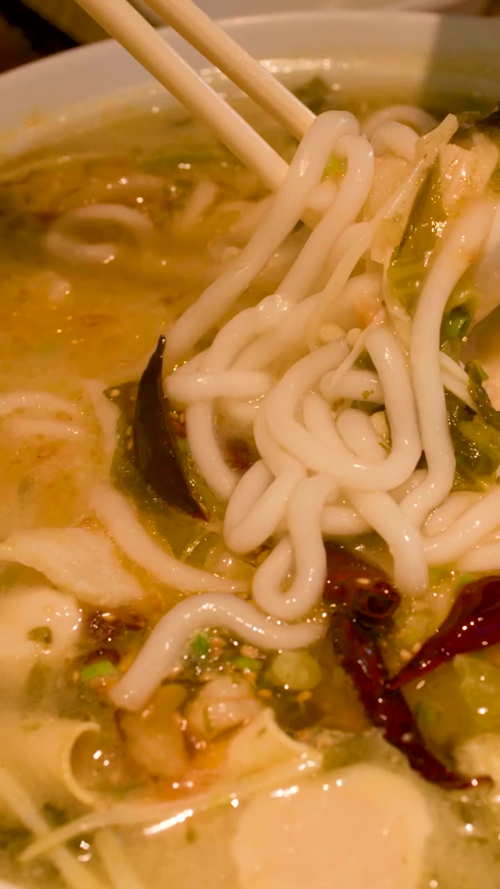Primo piano di bacchette che sollevano spaghetti di riso da un brodo piccante con polpette di pesce e peperoncini