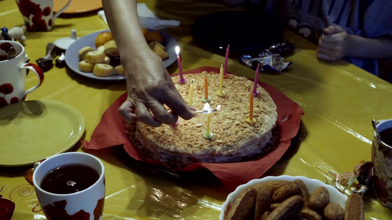 mamá y los niños celebran un cumpleaños y encenden velas en el pastel, que está en un mantel amarillo, en una servilleta roja.