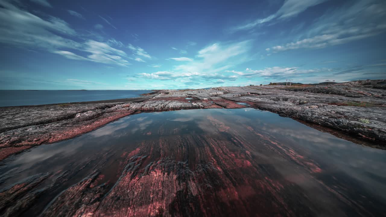 las nubes que pasan se reflejan en las aguas tranquilas de las piscinas de la marea en la costa rocosa