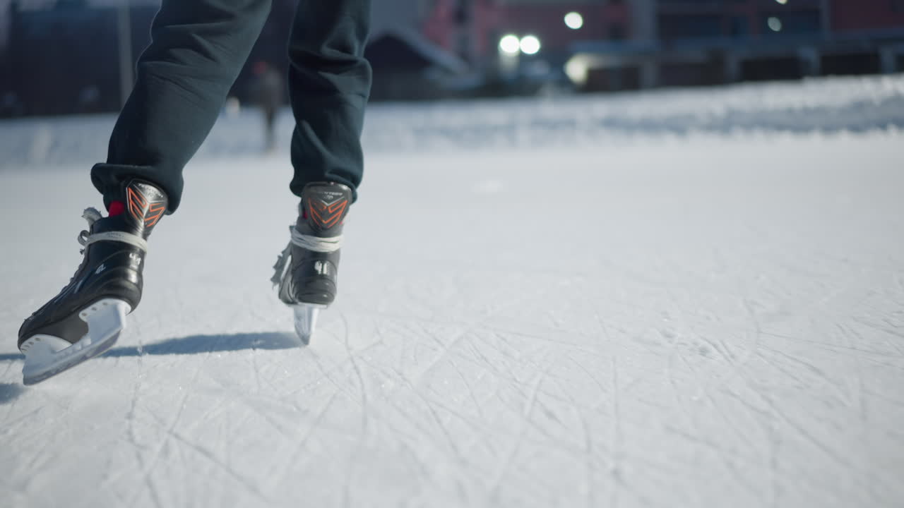 skaters gliding on ice rink during evening with bright lights illuminating scene visible long shadows cast on icy surface from black skating boots blur of people and buildings in background
