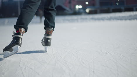 skaters gliding on ice rink during evening with bright lights illuminating scene visible long shadows cast on icy surface from black skating boots blur of people and buildings in background
