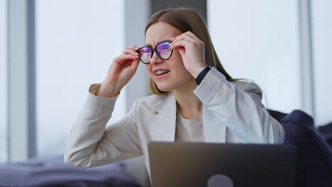 cheerful lady sits with laptop in front of her. woman is interested in something aside and puts on the glasses to see it better.