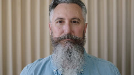 close up portrait of mature caucasian man stylish beard looking focused intense at camera serious pensive male wearing blue shirt