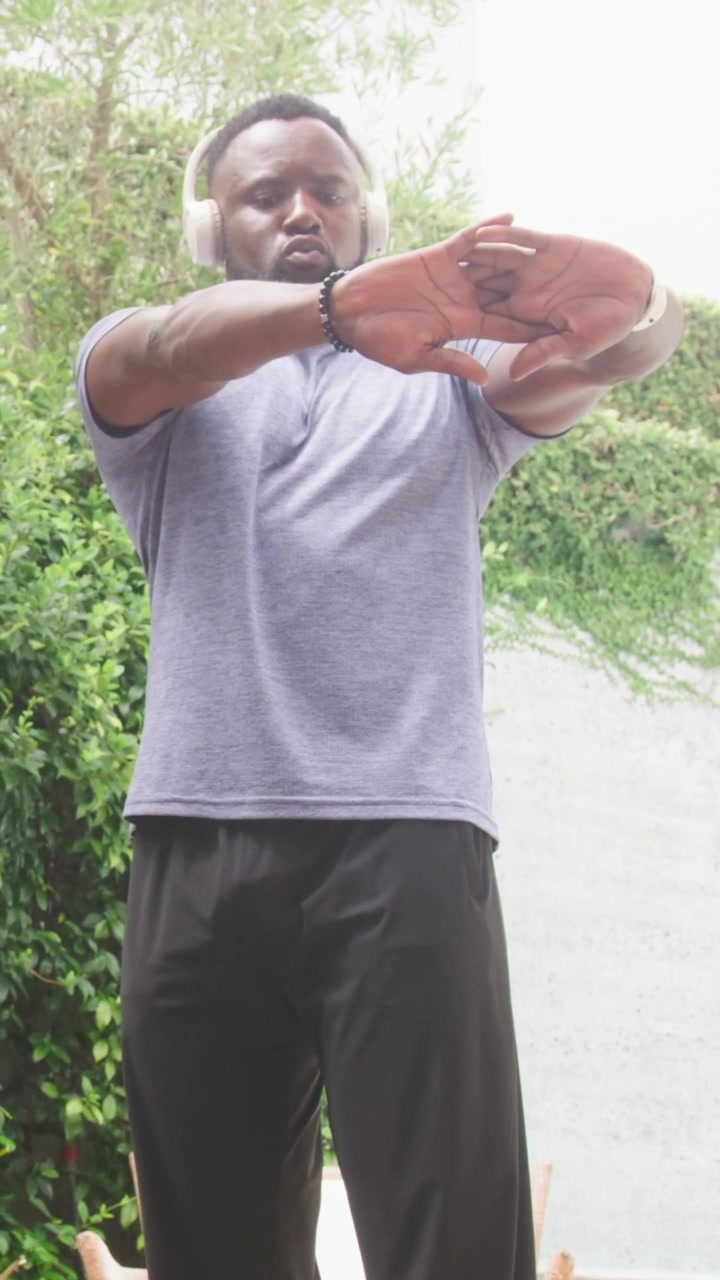 Vertical video: Stretching man after watch alert, warming up in garden wearing gym tee, headphones