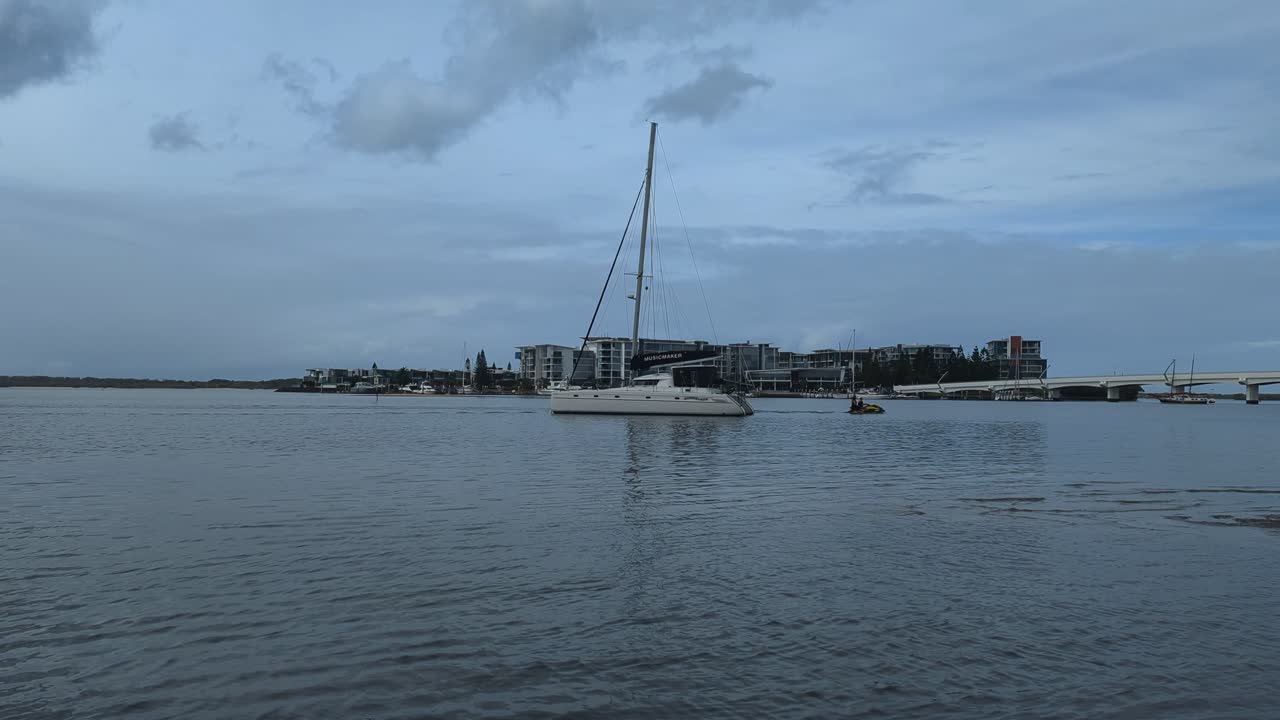 Catamaran in view on the rippling water with a jetski going past.