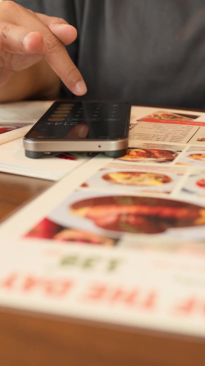 Person peger på menuen, bruger smartphone-lommeregner til at vælge mad i varm restaurantbelysning.