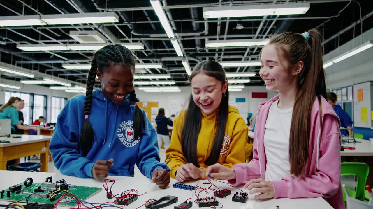 High-angle video shot of three girls in a tech classroom, engaged in hands-on electronics projects