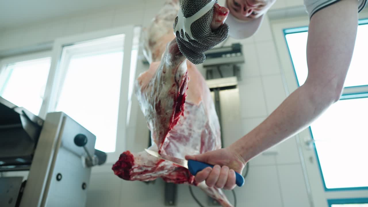 Butcher Carving Up Lamb Hanging From Hook