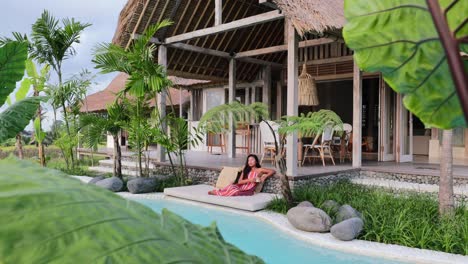 wide slow motion of female lounging at private pool next to bohemian villa in bali indonesia