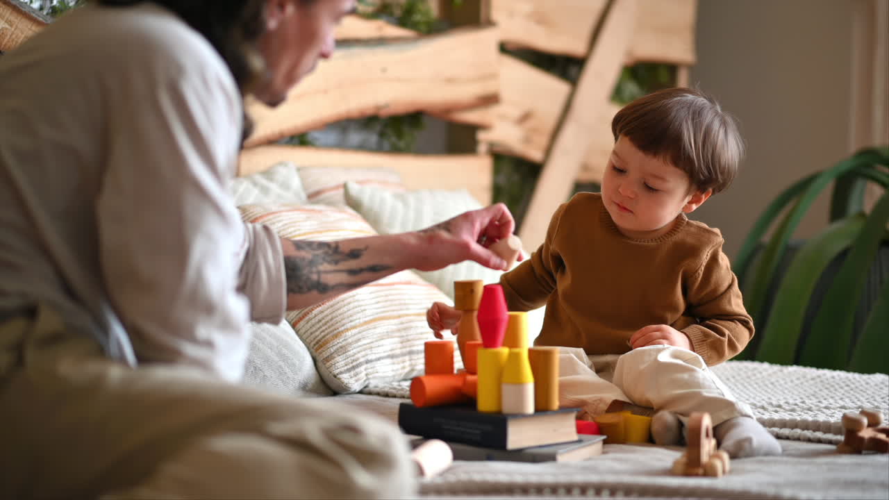 Father playing with his son with colourful, ecological wooden toys on the bed