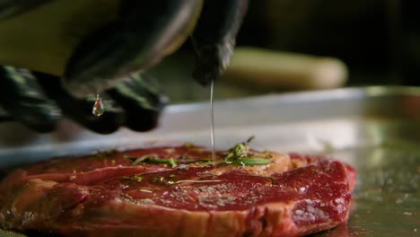 Chef-squirts-and-rubs-olive-oil-into-beautiful-cut-of-steak-with-herbs-on-metal-tray