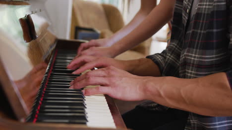 close up of diverse couple playing piano at home together