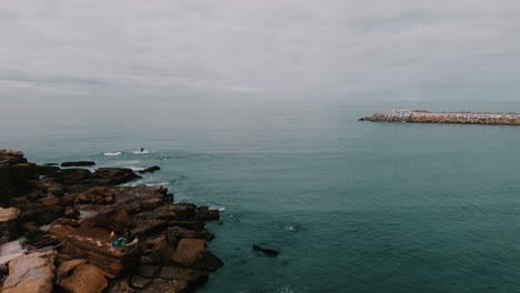 Overtake-Shot-Of-Man-Playing-Berimbau-The-Brazilian-Musical-Instrument-In-Front-Of-Cloudy-Blue-Ocean,-Ericeira,-Portugal