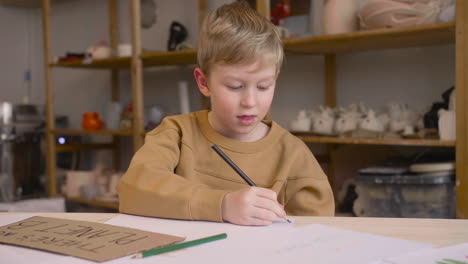 Niño-Rubio-Dibujando-Sentado-En-Una-Mesa-En-Un-Taller-De-Artesanía