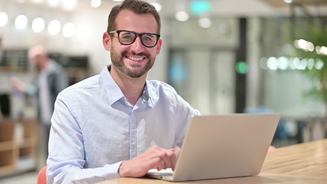 Businessman with Laptop Smiling at Camera in Office