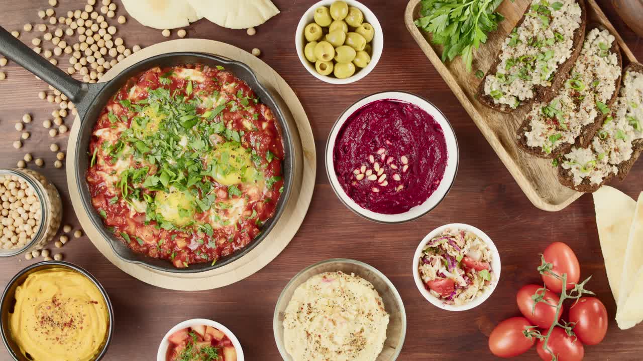 cocina tradicional israelí. shakshuka en sartén decorado con perejil, hummus en la mesa, poniendo forshmak. platos nacionales judíos vista superior. huevos fritos en salsa de tomate, salsa, pita, cultura de oriente medio