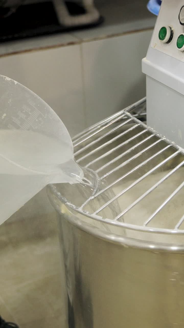 Baker Pouring Water into Flour in Industrial Dough Mixer