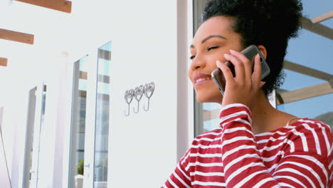 Side-view-of-young-mixed-race-woman-talking-on-mobile-while-sitting-in-balcony-at-home-4k