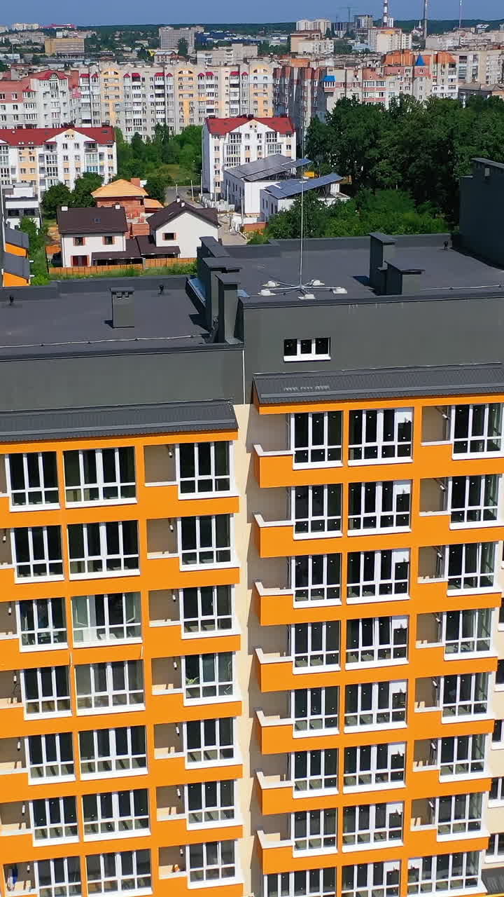 New city landmark. Modern apartment building on urban background. Colorful design of a multi-storey architecture. Aerial view. Vertical video