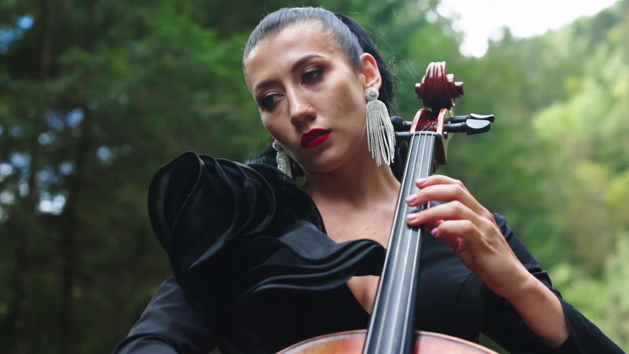 Girl performing music outdoor. Musician playing on cello on mountain nature