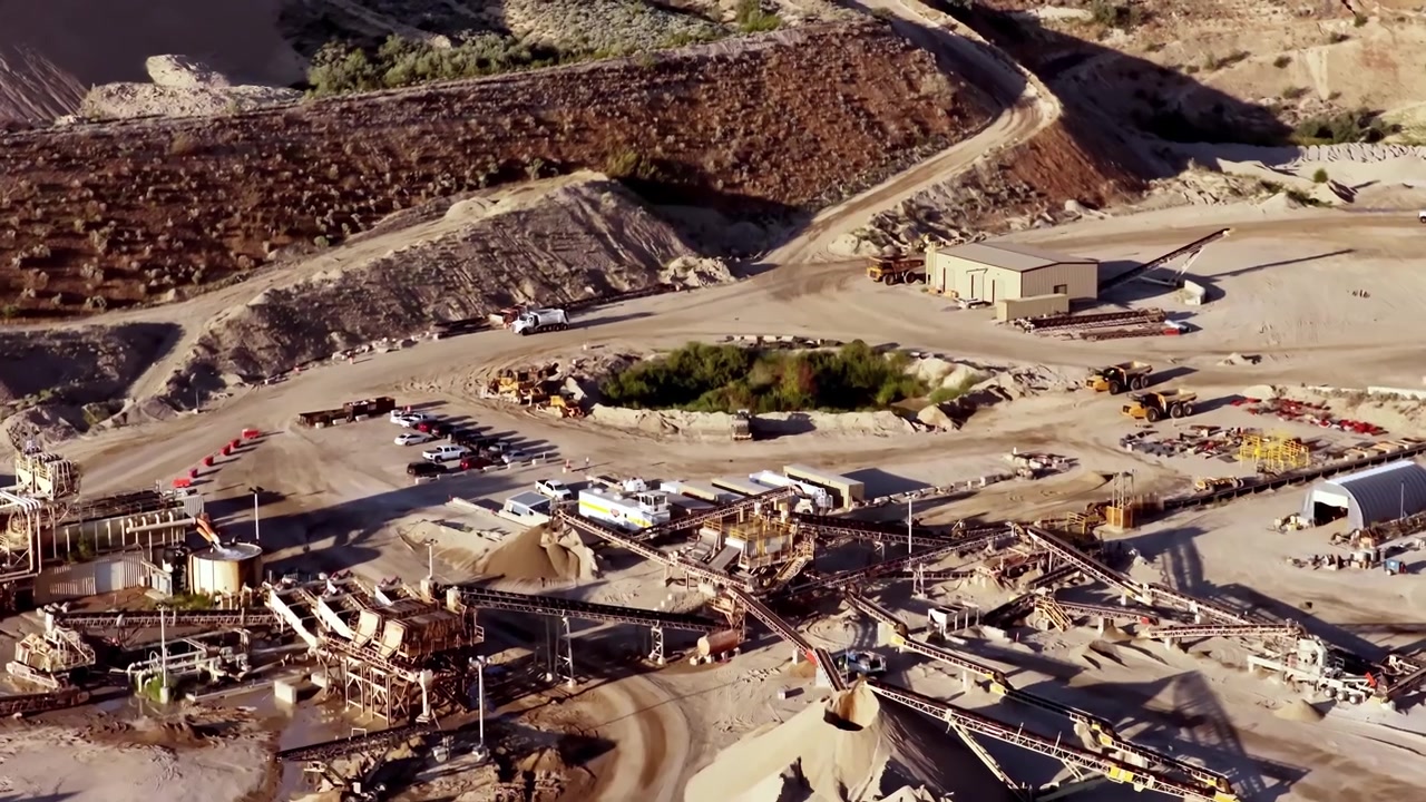 An industrial gravel and sand aggregate pit mine, screw washers, working conveyor belts, rugged terrain, and golden hour sunlight casting striking shadows - aerial flyover.