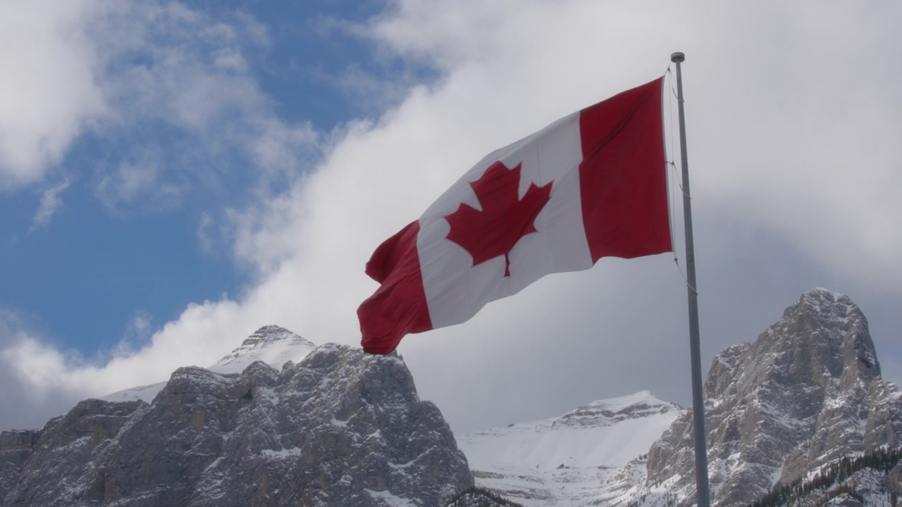 Bandiera canadese contro il cielo blu e le Montagne Rocciose innevate