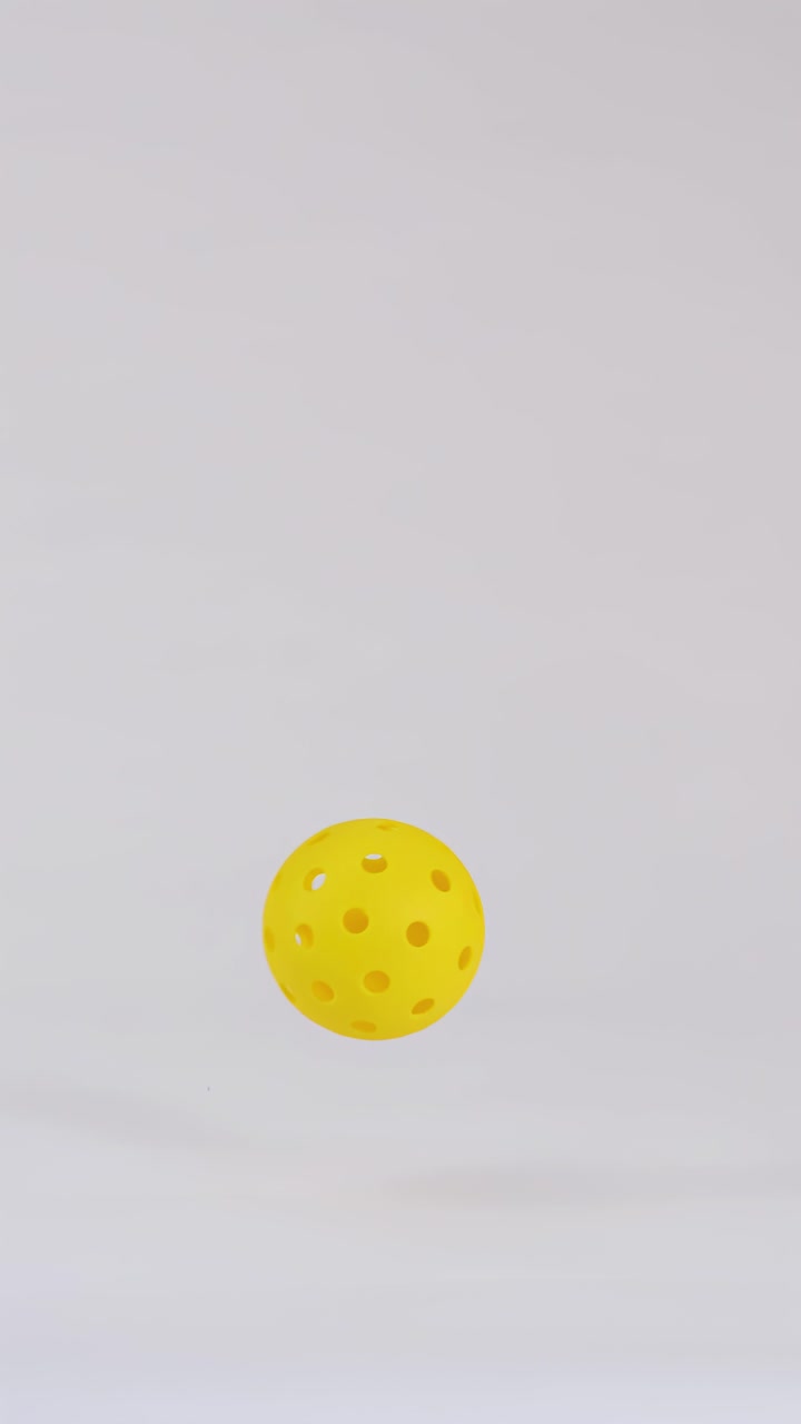 A single yellow pickleball falls vertically and bounces on a white surface in slow motion
