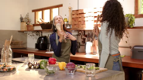 two multiracial female friends laughing and cooking together in kitchen, at home